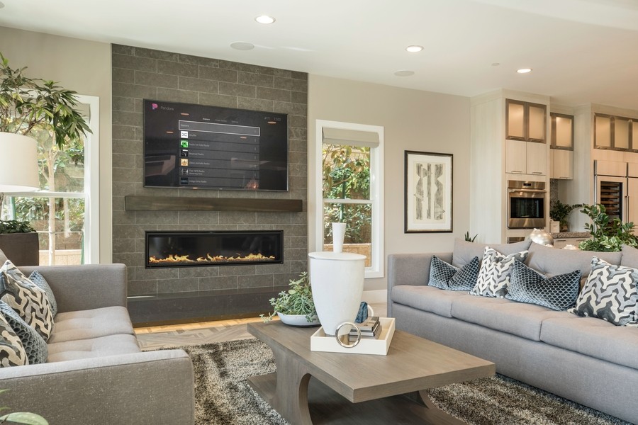 Stylish modern living room featuring a wall-mounted TV above a stone fireplace surrounded by comfortable gray sofas adorned with patterned pillows.