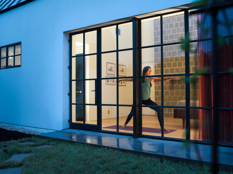 A person doing yoga asanas is seen through a home’s windows illuminated by Ketra Lighting.