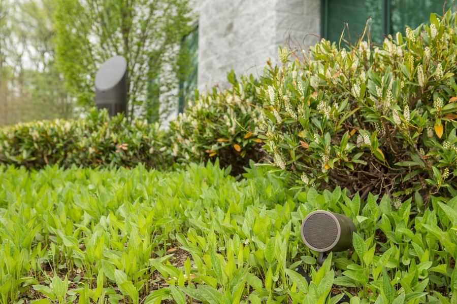 outdoor speakers installed in the landscape of a home with green leafy bushes