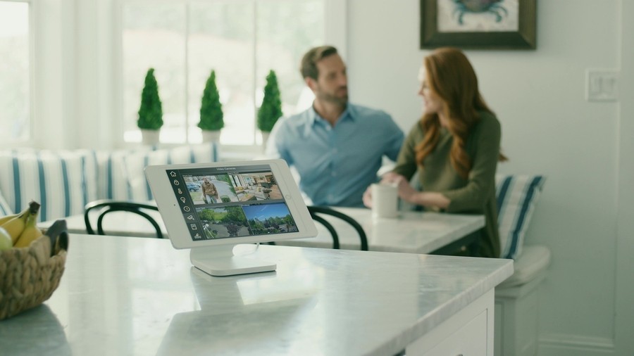 a couple sitting on a sofa with an Elan control panel sitting on a kitchen counter