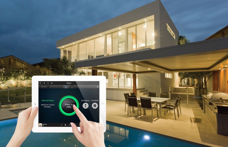 A well-lit home with a pool in the backyard and an overlayed image of hands arming the alarm on a Control4 touchscreen.