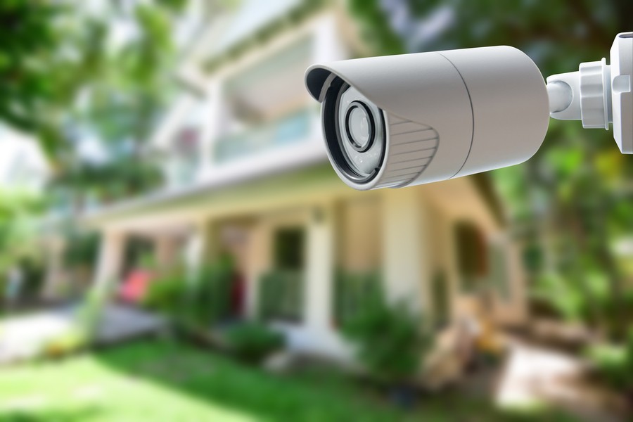 Image is of a home surveillance camera in the foreground with a house in the background.