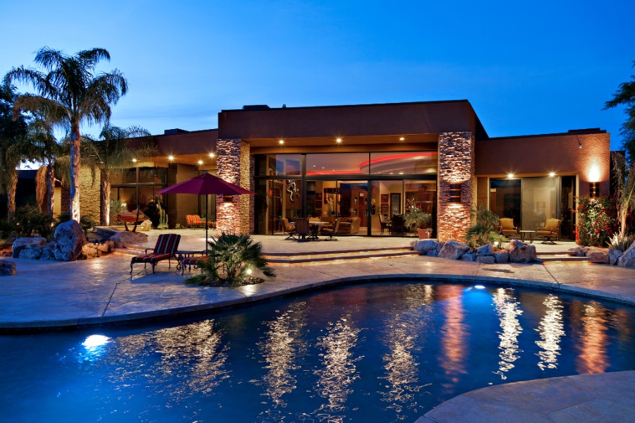 A nighttime view of a large modern home with a pool. 