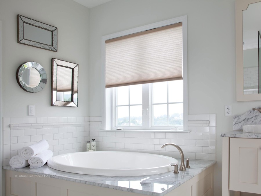 A luxury bathroom with motorized shades drawn halfway down above a large bathtub.