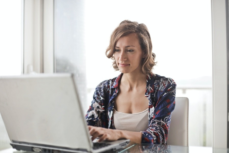 A woman working at a home office with motorized shades in the background.